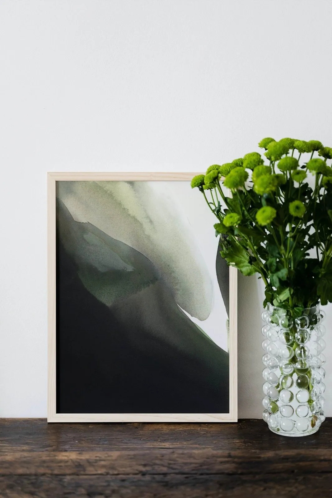 Green and black abstract painting leaning beside a vase of green flowers