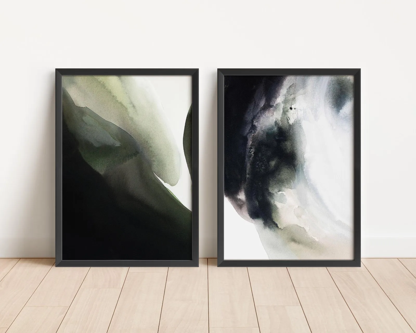 Two green and black abstract paintings in black frames on a wooden floor