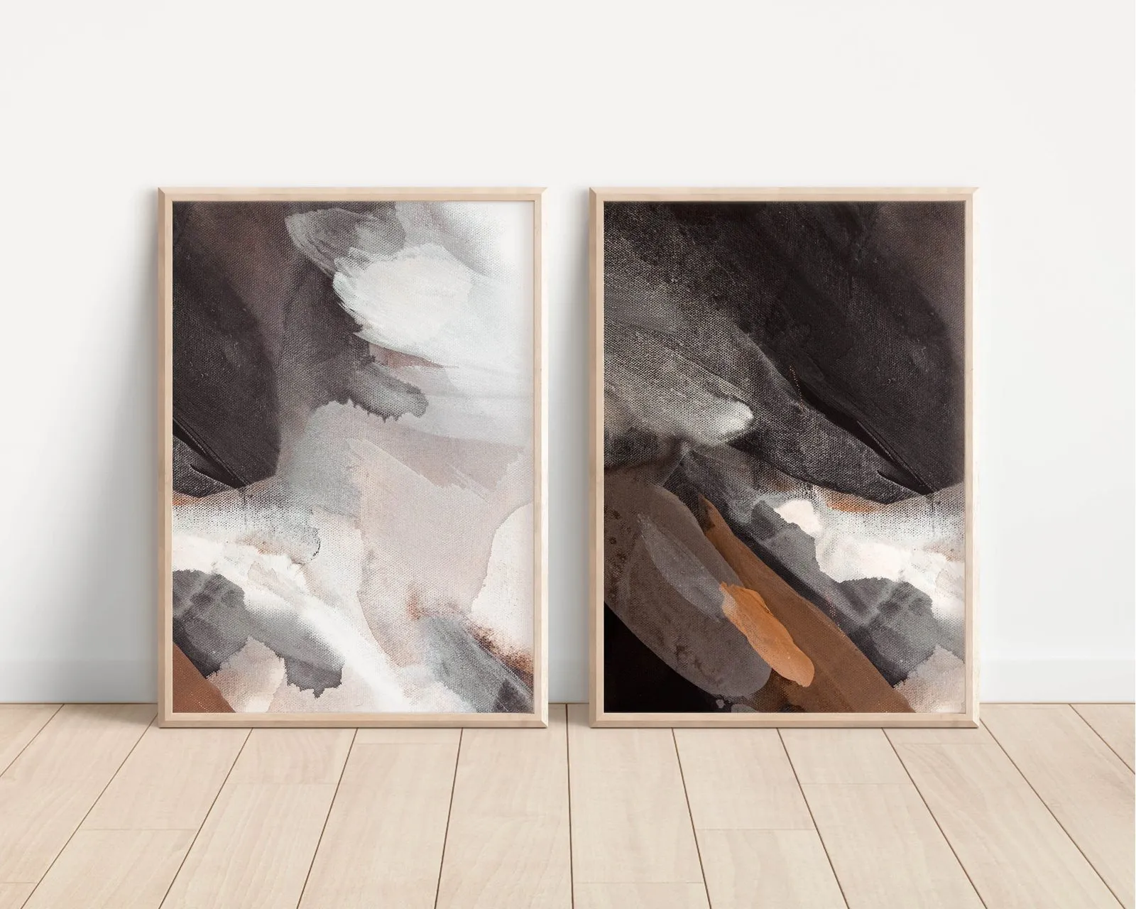 Two abstract paintings in brown and grey leaning against a white wall